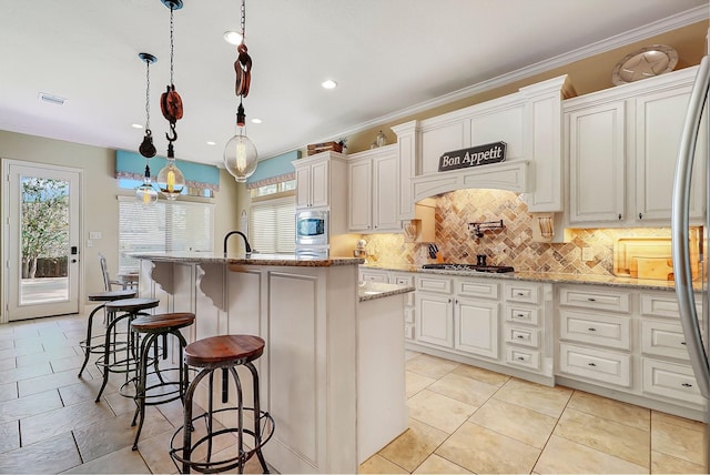 kitchen with pendant lighting, a kitchen island with sink, white cabinets, light stone countertops, and a kitchen bar