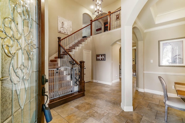 entryway featuring arched walkways, crown molding, a high ceiling, an inviting chandelier, and baseboards