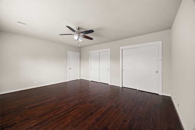 unfurnished bedroom featuring multiple closets, ceiling fan, and dark hardwood / wood-style flooring