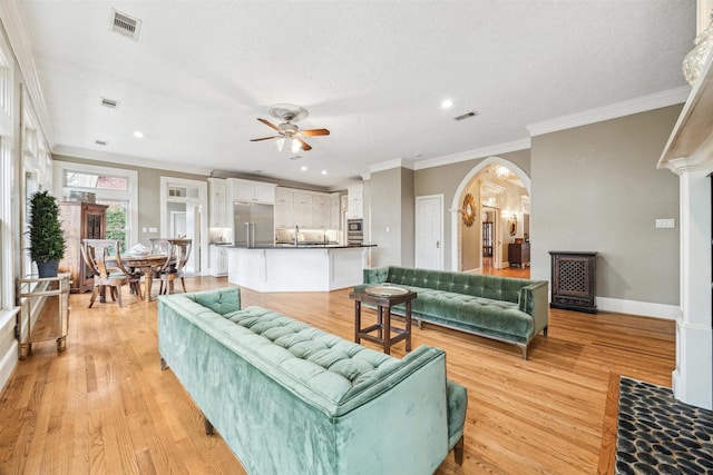 living room with ceiling fan, ornamental molding, light hardwood / wood-style flooring, and a textured ceiling