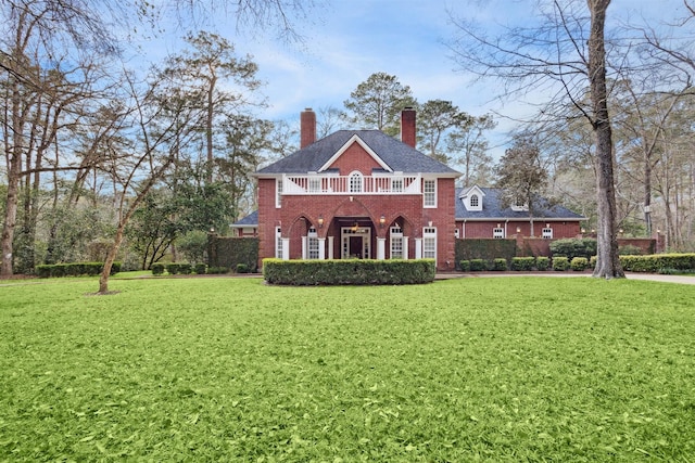 exterior space with brick siding, a chimney, a front yard, and a balcony