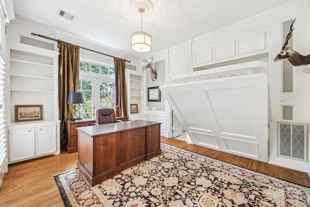 office space with built in shelves, a textured ceiling, and light hardwood / wood-style flooring