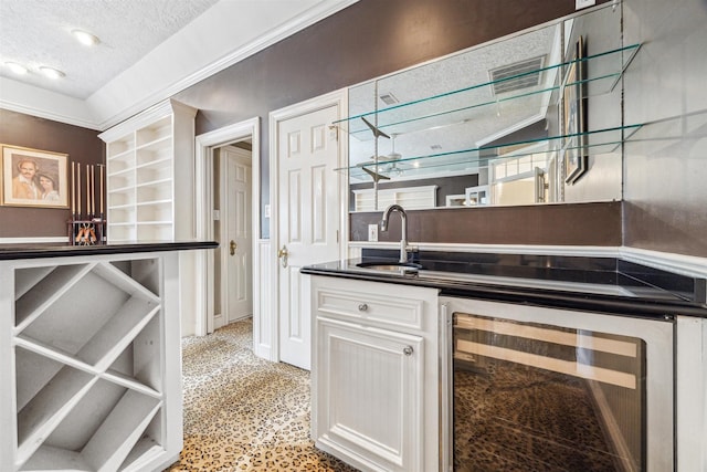 bar featuring white cabinets, sink, beverage cooler, and a textured ceiling