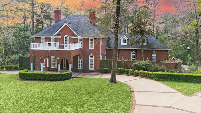 colonial home featuring brick siding, curved driveway, a chimney, and a front lawn