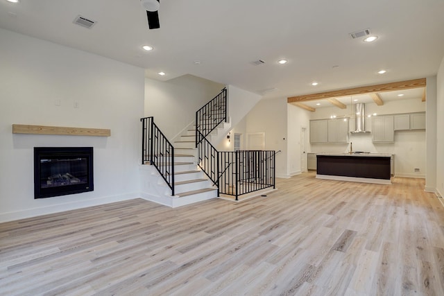 unfurnished living room with ceiling fan, light hardwood / wood-style floors, and beamed ceiling