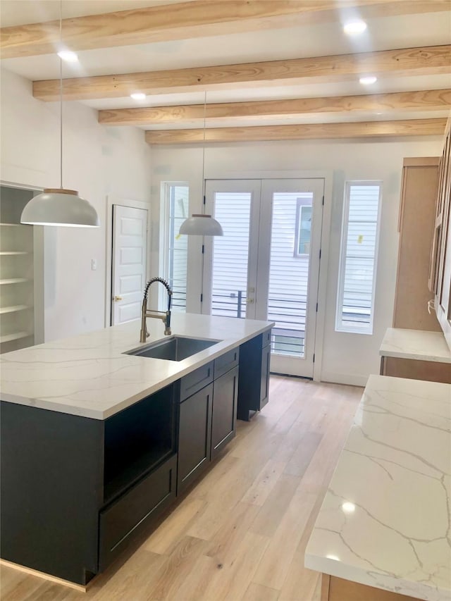 2215 Bevis St, Houston, TX 77008 - kitchen with beam ceiling, a kitchen island with sink, dark cabinets, light stone countertops, and light wood-style flooring