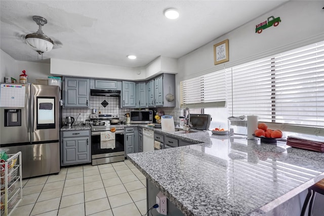 kitchen featuring stainless steel appliances, kitchen peninsula, light tile patterned floors, and backsplash