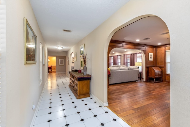 corridor with visible vents, arched walkways, baseboards, and wood finished floors