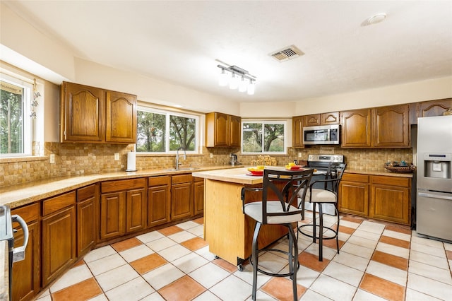 kitchen with a kitchen island, appliances with stainless steel finishes, brown cabinets, a kitchen breakfast bar, and light countertops