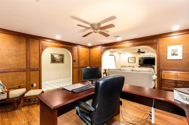 office area with arched walkways, ceiling fan, light wood finished floors, and visible vents