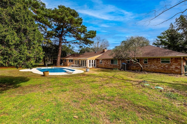 back of house featuring brick siding, an outdoor pool, and a lawn