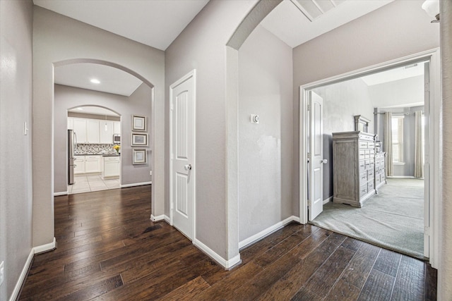 corridor with baseboards, arched walkways, and dark wood-type flooring