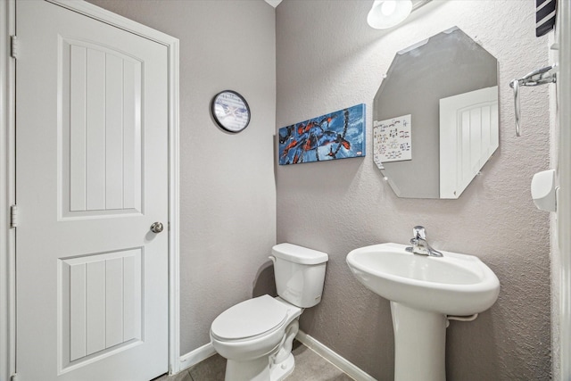 half bathroom featuring toilet, tile patterned flooring, baseboards, and a textured wall