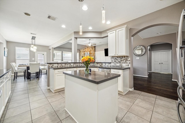 kitchen with a center island, decorative light fixtures, dark countertops, visible vents, and white cabinets