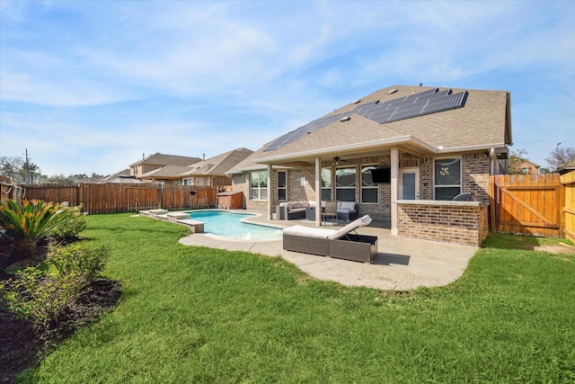 rear view of house with brick siding, a fenced backyard, a fenced in pool, and roof mounted solar panels