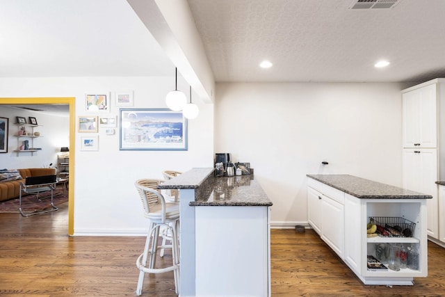 kitchen featuring hanging light fixtures, a breakfast bar, white cabinets, and dark stone counters