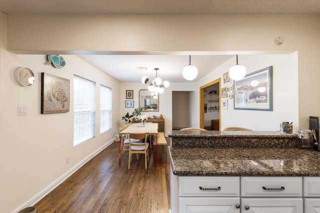 kitchen with dark stone countertops, hanging light fixtures, an inviting chandelier, dark hardwood / wood-style floors, and white cabinets