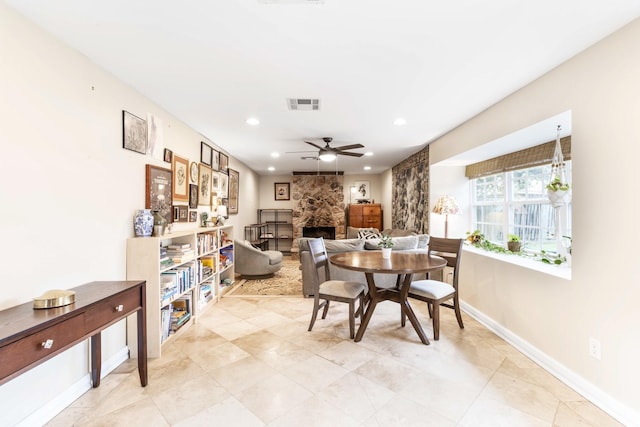 dining space with ceiling fan and a stone fireplace