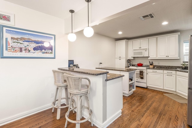 kitchen featuring a breakfast bar area, white cabinetry, decorative light fixtures, dark stone countertops, and white appliances