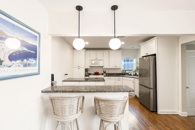 kitchen featuring a breakfast bar, white cabinetry, stainless steel fridge, kitchen peninsula, and dark hardwood / wood-style floors