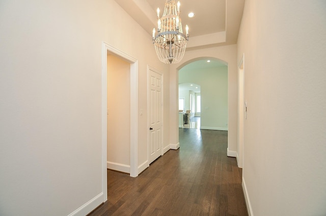 hallway featuring dark wood-type flooring, a chandelier, and a tray ceiling