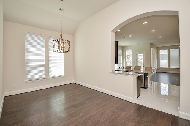 unfurnished dining area featuring dark wood-type flooring, lofted ceiling, and a chandelier