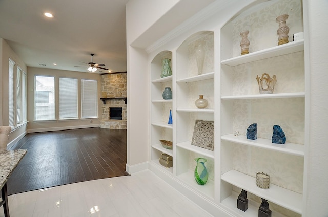 interior space with a stone fireplace, built in shelves, ceiling fan, and hardwood / wood-style flooring