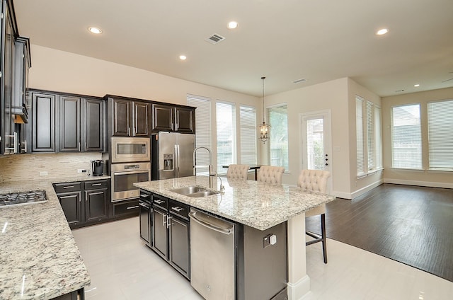 kitchen with stainless steel appliances, light stone countertops, sink, and a center island with sink