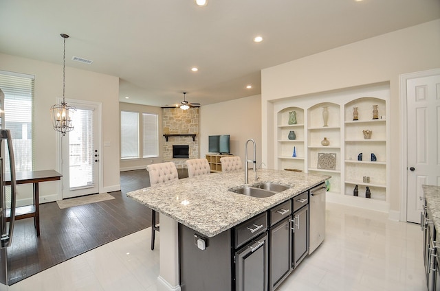 kitchen featuring dishwasher, sink, a kitchen bar, hanging light fixtures, and a center island with sink