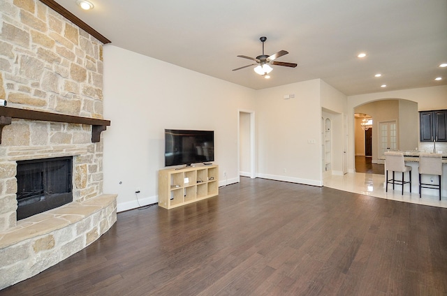 unfurnished living room featuring dark hardwood / wood-style flooring, a stone fireplace, and ceiling fan