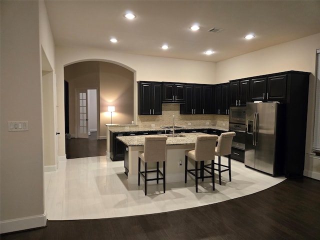 kitchen with a breakfast bar area, light stone counters, stainless steel appliances, a center island with sink, and light hardwood / wood-style flooring