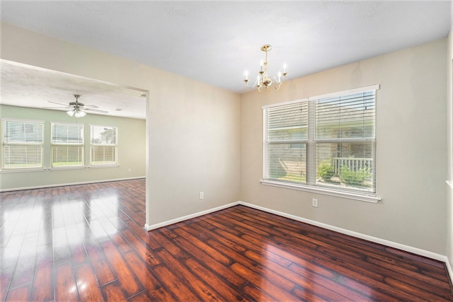 spare room with ceiling fan with notable chandelier, dark wood-style flooring, and baseboards