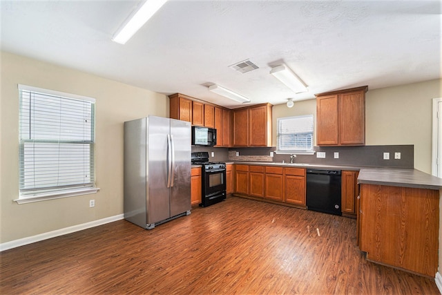 kitchen with dark wood finished floors, visible vents, brown cabinetry, a sink, and black appliances