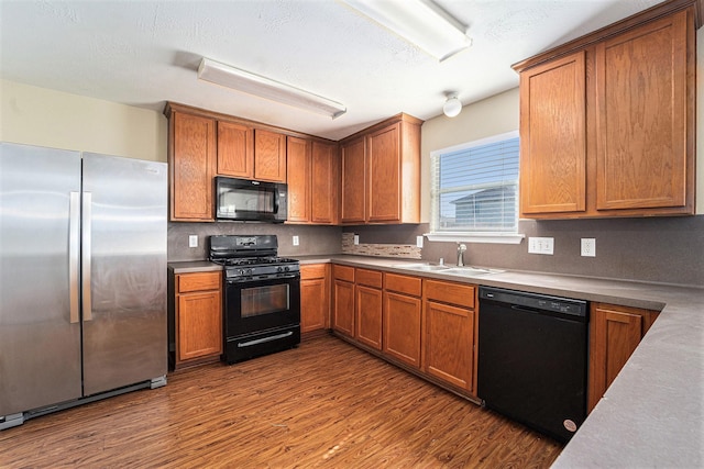 kitchen featuring black appliances, a sink, light countertops, and brown cabinets