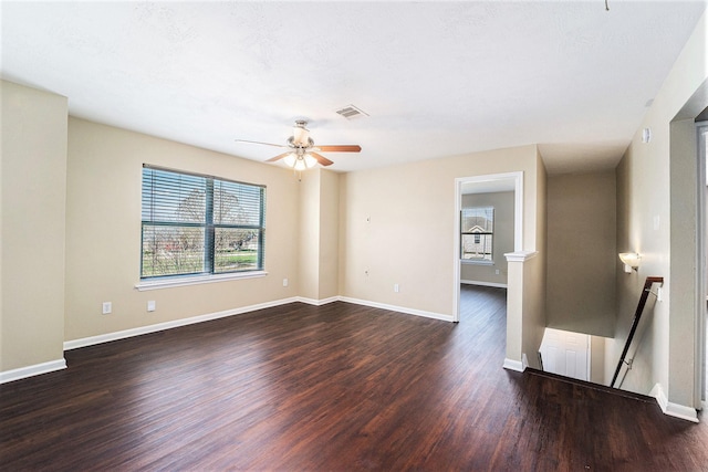 empty room featuring a ceiling fan, dark wood finished floors, visible vents, and baseboards