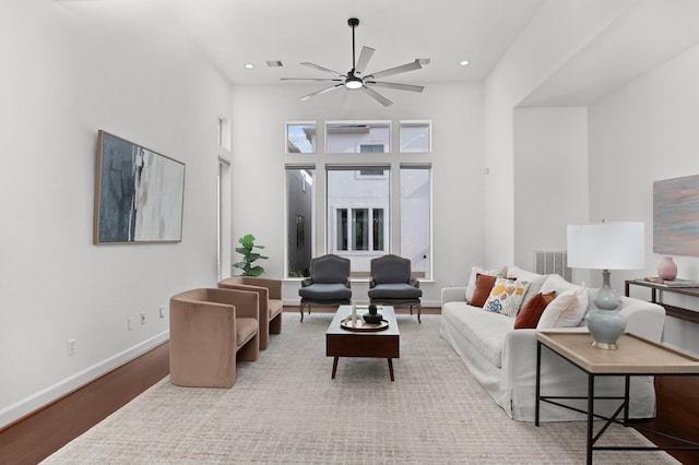 living room featuring ceiling fan, light hardwood / wood-style flooring, and a high ceiling