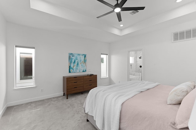 bedroom with ceiling fan, light colored carpet, a tray ceiling, and ensuite bath