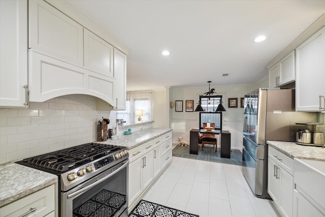 kitchen with crown molding, appliances with stainless steel finishes, white cabinetry, light stone counters, and tasteful backsplash