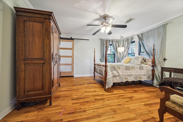 bedroom with ceiling fan, ornamental molding, a barn door, and light wood-type flooring