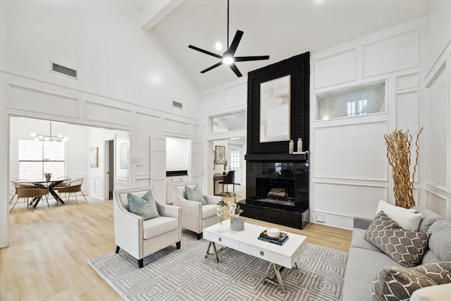 living room featuring high vaulted ceiling, light wood-type flooring, a large fireplace, beamed ceiling, and ceiling fan with notable chandelier