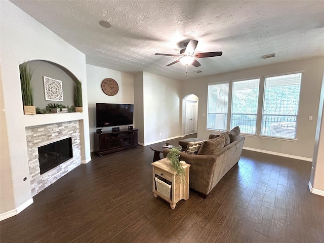 living room with a stone fireplace, dark hardwood / wood-style floors, a textured ceiling, and ceiling fan