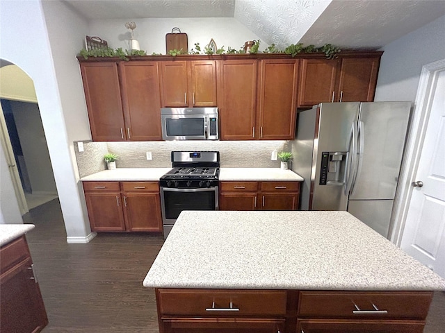 kitchen featuring appliances with stainless steel finishes, tasteful backsplash, a textured ceiling, dark hardwood / wood-style flooring, and vaulted ceiling