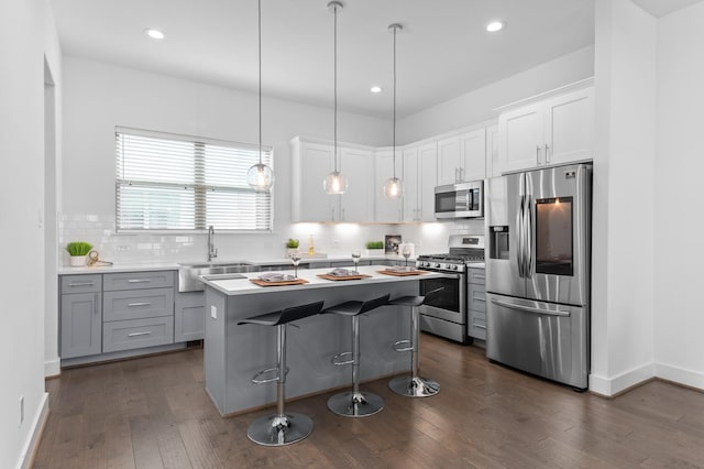 kitchen with sink, hanging light fixtures, a kitchen island, stainless steel appliances, and white cabinets