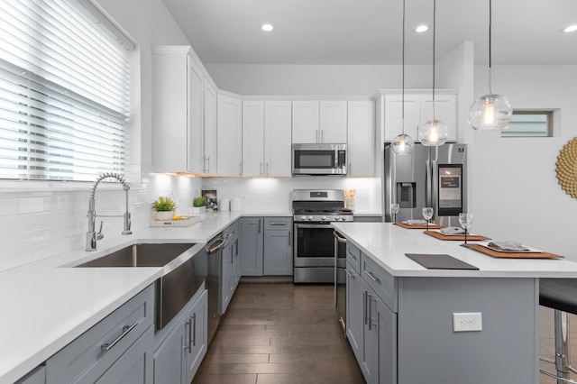 kitchen with gray cabinets, appliances with stainless steel finishes, decorative light fixtures, sink, and a kitchen bar