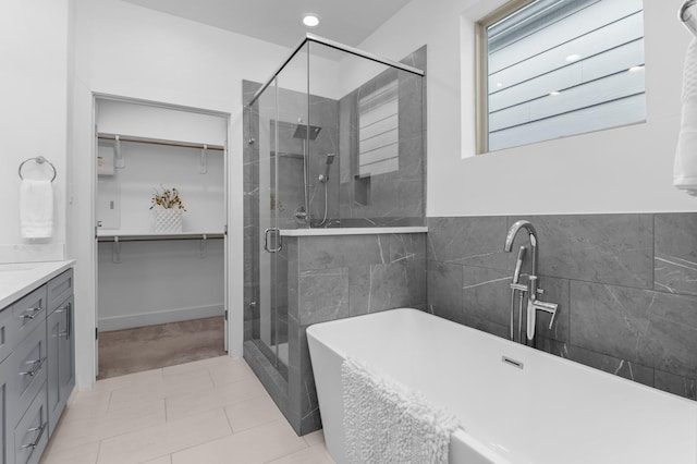 bathroom with independent shower and bath, vanity, tile patterned flooring, and tile walls