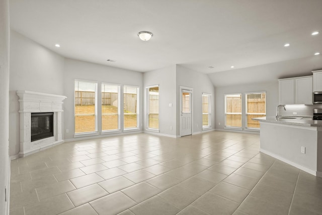 unfurnished living room with lofted ceiling, a high end fireplace, sink, and light tile patterned floors