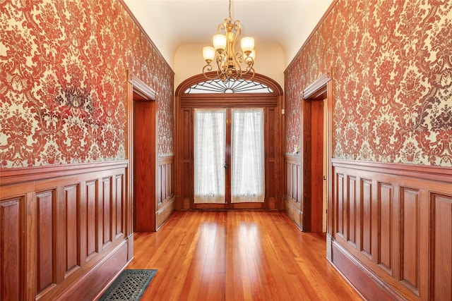 1428 Ball, Galveston, TX 77550 - entrance foyer with wallpapered walls, a chandelier, light wood-type flooring, a wainscoted wall, and french doors