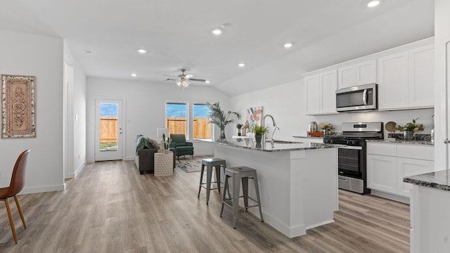 kitchen with sink, appliances with stainless steel finishes, white cabinetry, a kitchen island with sink, and dark stone counters