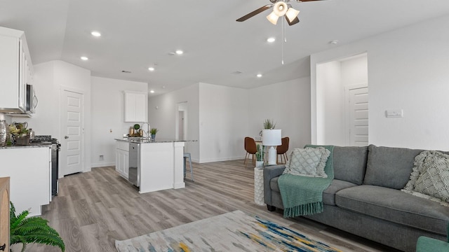 living room with ceiling fan, lofted ceiling, and light wood-type flooring