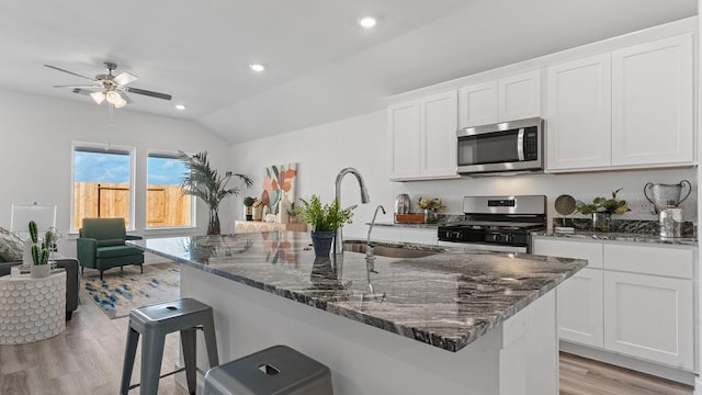 kitchen with a breakfast bar area, white cabinetry, stainless steel appliances, a center island with sink, and dark stone counters